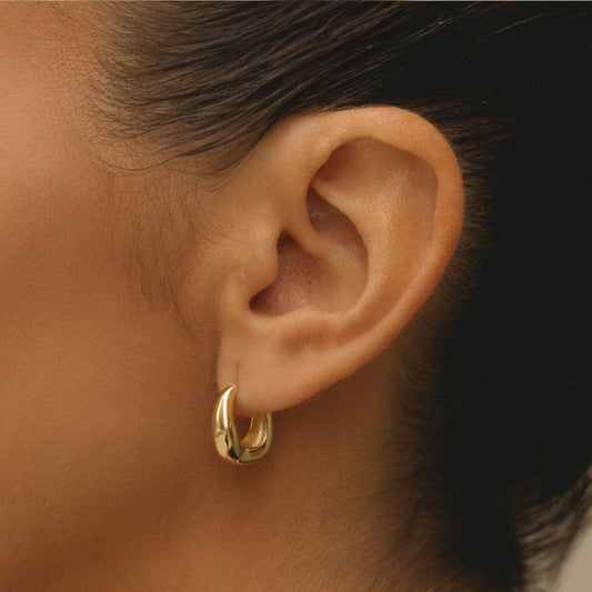 Gold wavy hoop earring on ear, glossy curved design