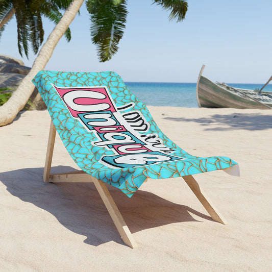 Turquoise mermaid-scale beach towel draped on a chair with large colorful slogan