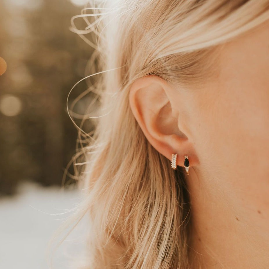 Gold diamond hoop earring worn beside a dark gemstone stud