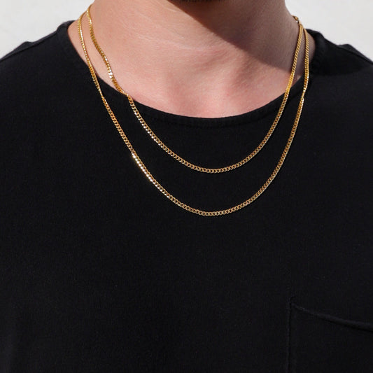 Gold Cuban link chain necklace layered on a model’s neck over a black shirt.
