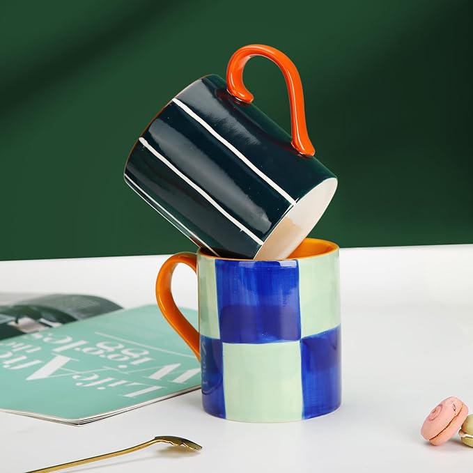 Stacked ceramic mugs with dark striped top and blue-mint checkered bottom, both with orange handles
