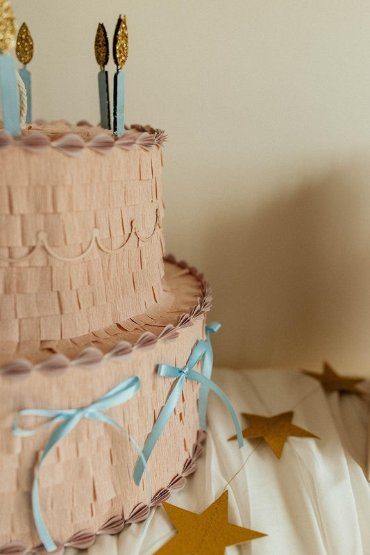 Piñata pastel rosa de dos pisos con lazos azules y estrellas doradas colgantes