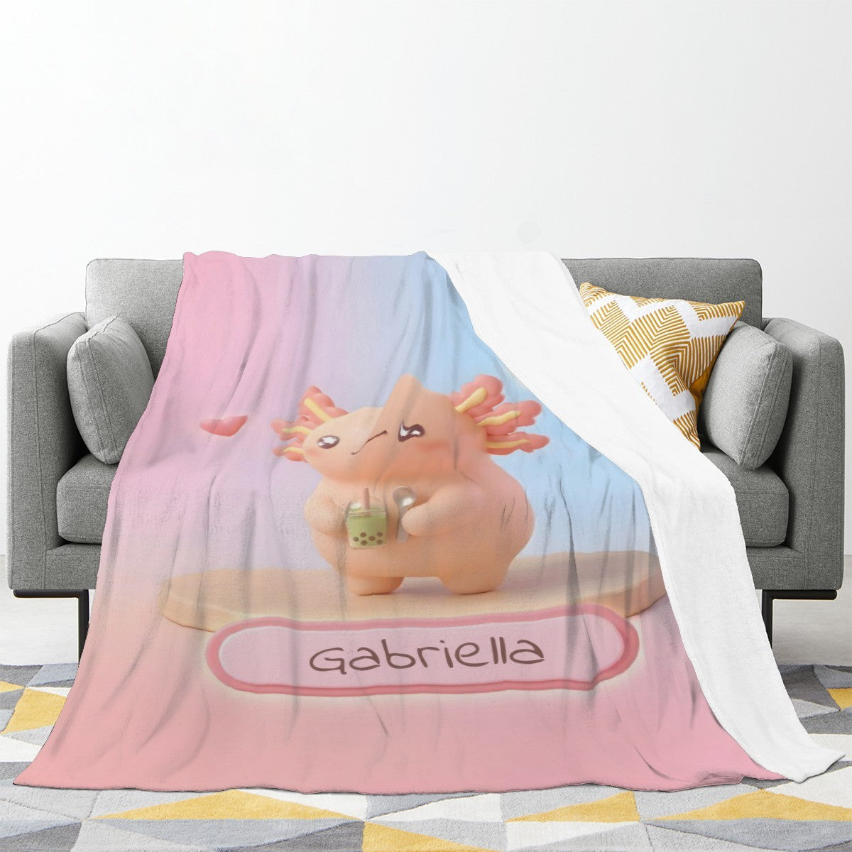 Large pink and light-blue character blanket draped over couch with “Gabriella” print
