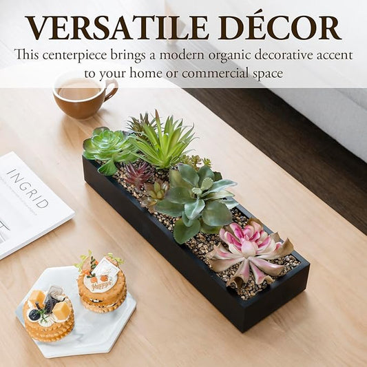 Black faux succulent planter box on a tabletop with green and pink plants