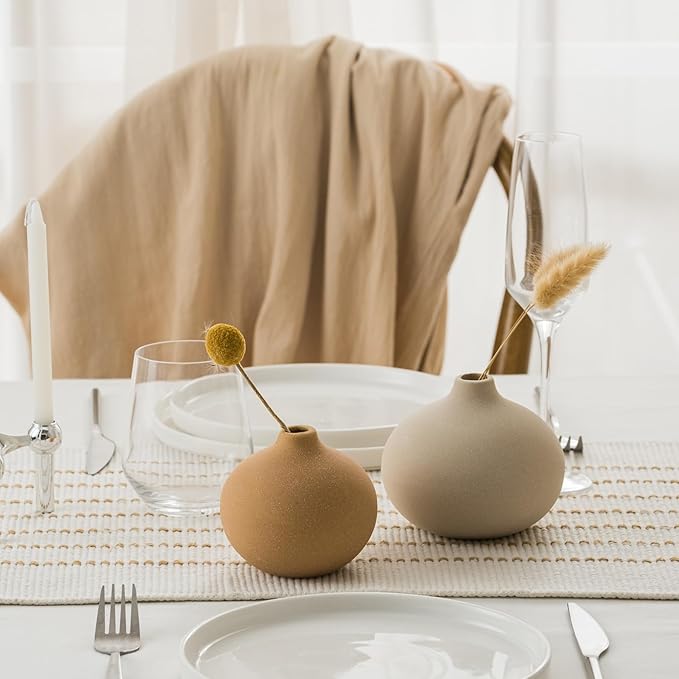 Matte ceramic bud vases with dried stems on a dining table setting