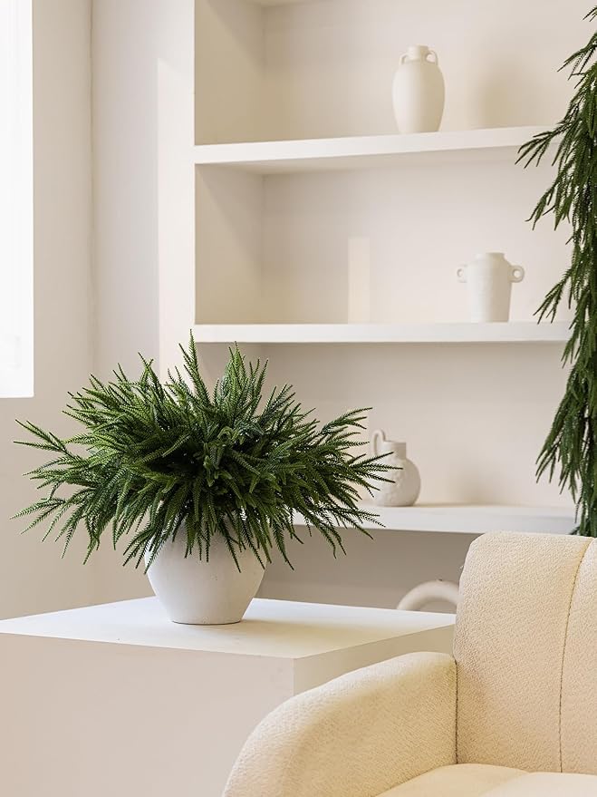 Artificial Norfolk pine branches arranged in a white vase on a table