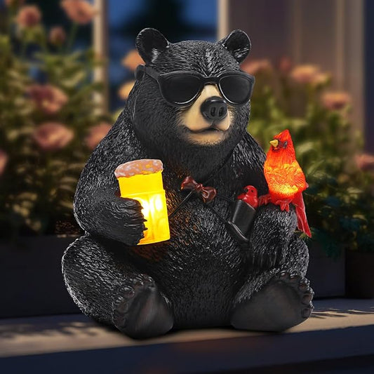 Black resin bear statue with sunglasses holding a glowing lantern and two red cardinals