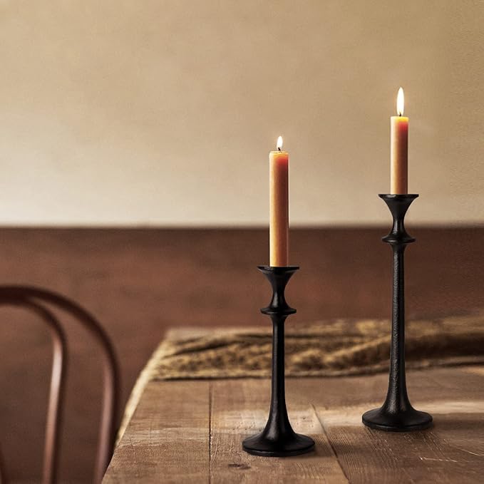 Two black iron taper candle holders with lit candles, standing on a wooden surface