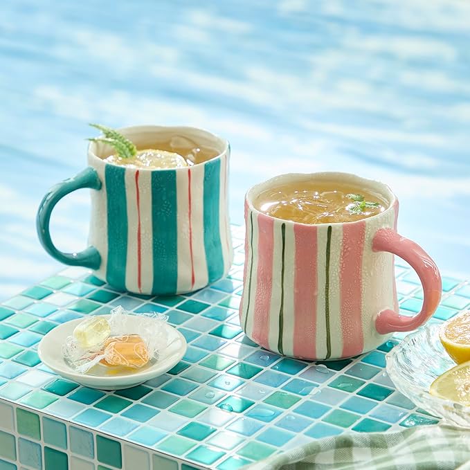 Two striped ceramic mugs on a turquoise tiled surface: pink and teal-green designs