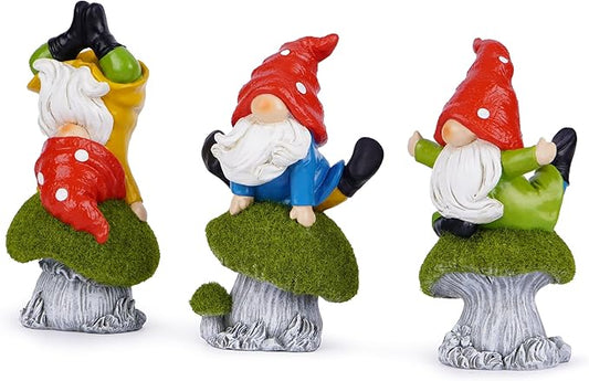 Three yoga gnome statues with red mushroom caps and green moss bases, posed in kneeling stretches