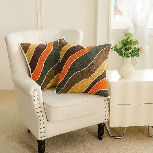 Tufted pillow cover with bold curved stripes in dark green, orange, tan, and brown