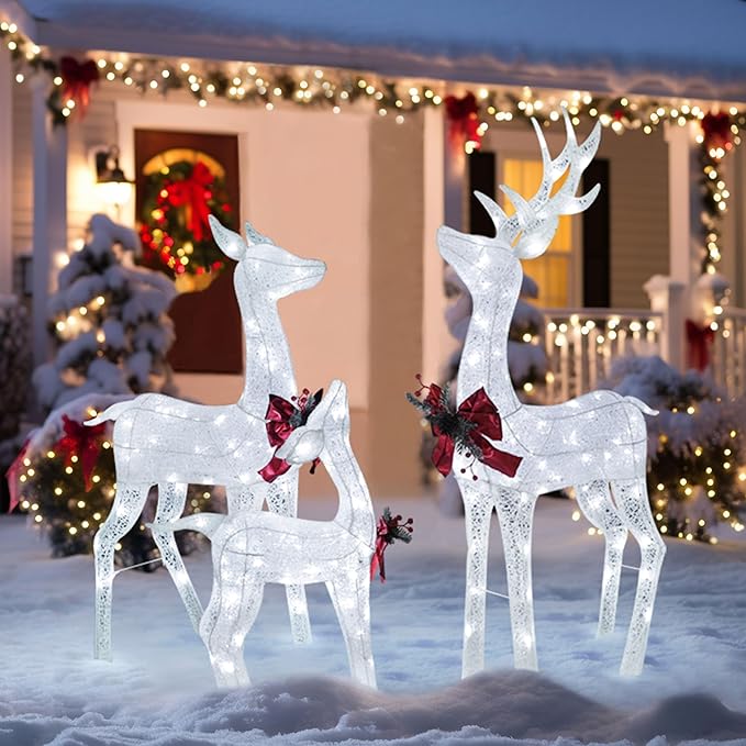 Three glittered white pre-lit reindeer decorations with red bows, standing in snow