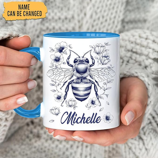 Blue-handled white mug held in hands, floral bee design with "Michelle" name