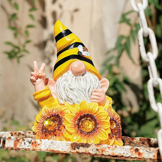 Bee-themed gnome solar statue in yellow-black hat with gray beard and lit sunflower flowers
