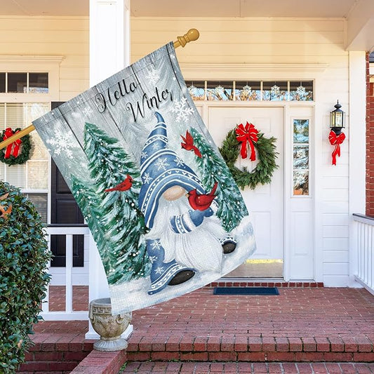 Winter gnome garden flag hanging on a porch, showing cardinals, pine trees, and snow scene