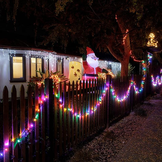 Outdoor fence line decorated with multicolor fairy string lights on green wire