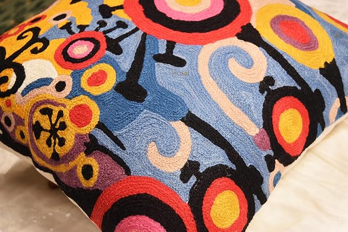 Decorative embroidered pillow cover with abstract swirl and ring motifs in blue, yellow, red, and black.