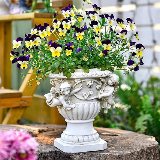 White resin angel urn planter with cherub figures, holding yellow and purple flowers