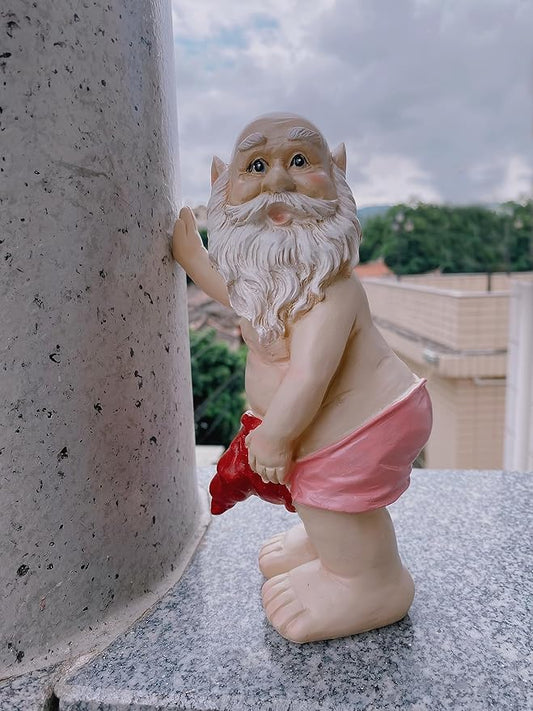 Garden gnome statue leaning against wall, white beard, pink shorts, raised hand