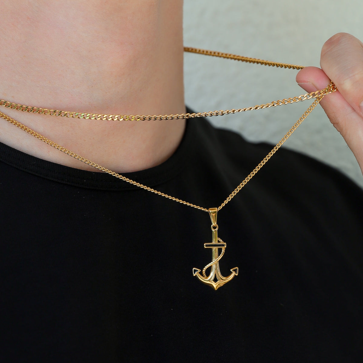 Gold anchor pendant Cuban link necklace set, chain held near pendant detail
