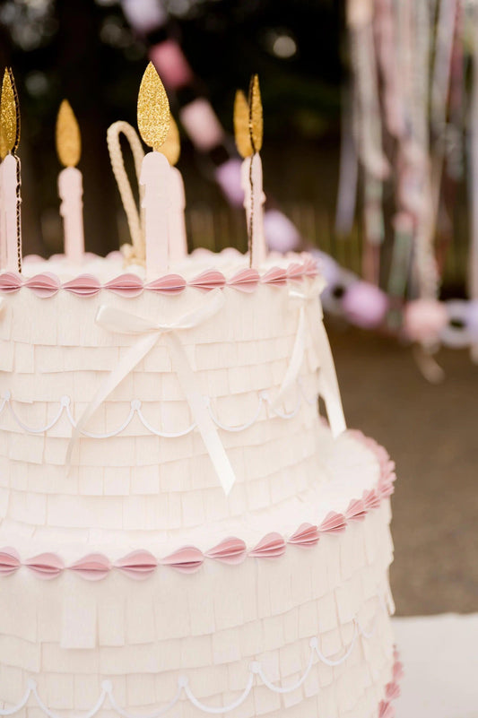 Piñata pastel blanca con detalle de velas doradas y borde rosa
