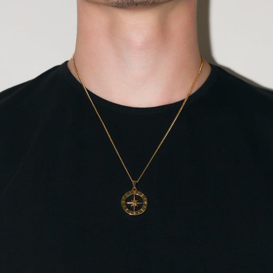 Gold compass pendant necklace worn on neck over dark crewneck shirt