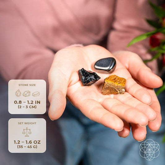 Hand holding three small stones: dark black, metallic gray, and gold-brown pieces.