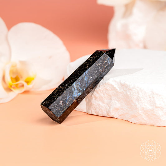 Gemstone crystal point, dark black with blue sparkle, on white cloth.
