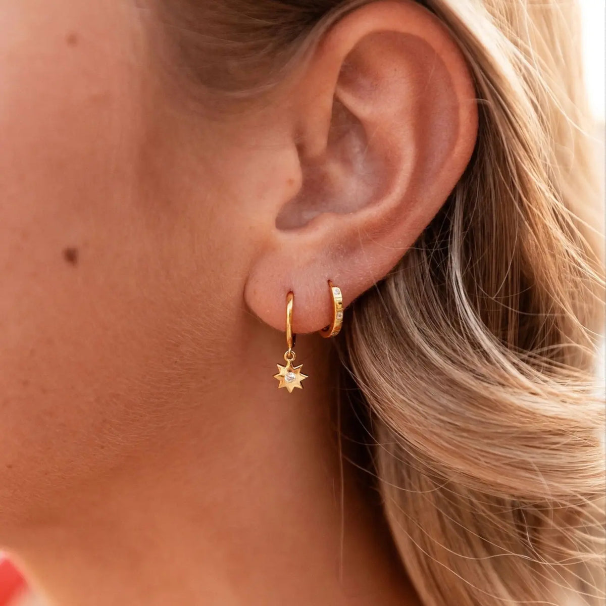 Gold vermeil huggie hoop and dangling sunburst charm, shown close up beside another hoop.