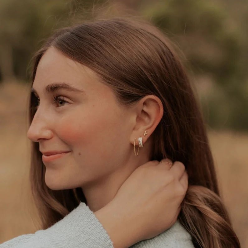 Gold twist hoop earring worn with a small stud