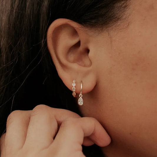 Gold teardrop stone hoop earrings shown worn on an ear.