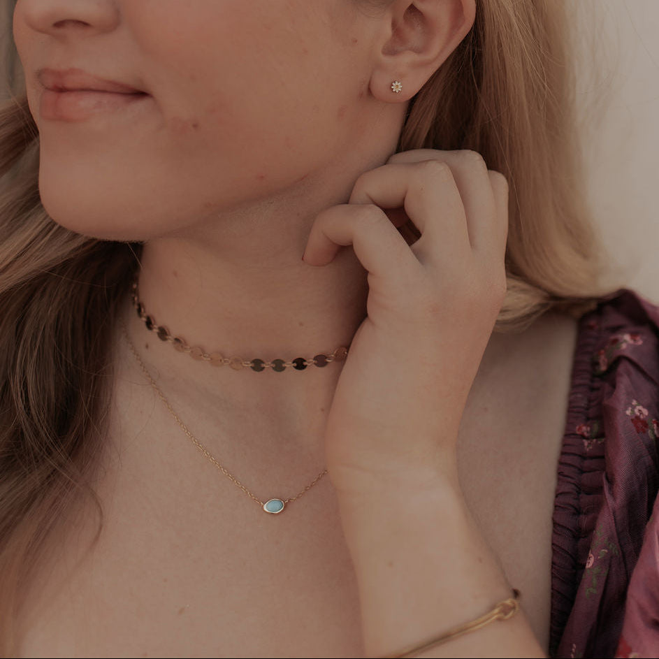 Fine chain necklace with a small oval turquoise-colored pendant, worn layered