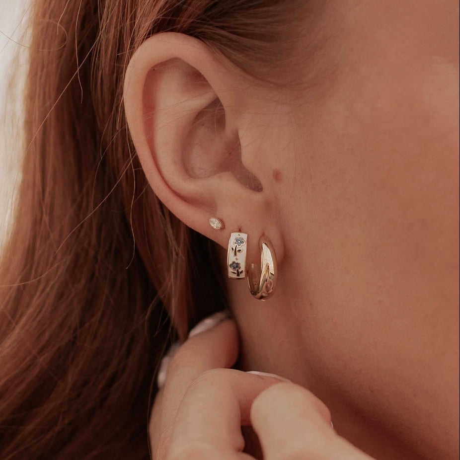 Gold-toned floral enamel hoop earring worn below a stud