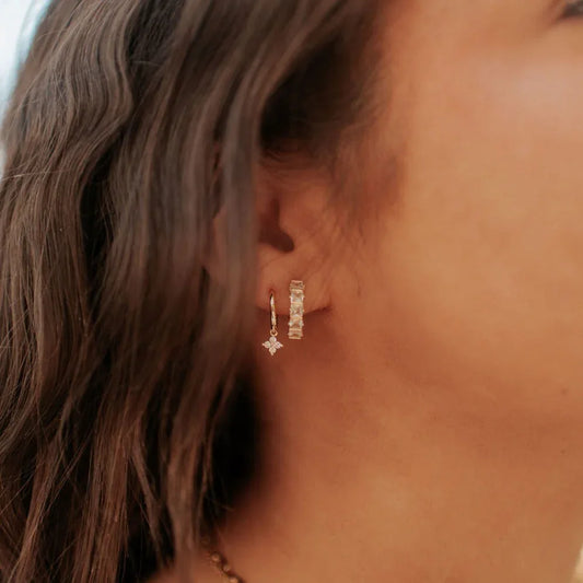 Gold hoop with a dangling flower charm, shown beside a slim rectangular earring