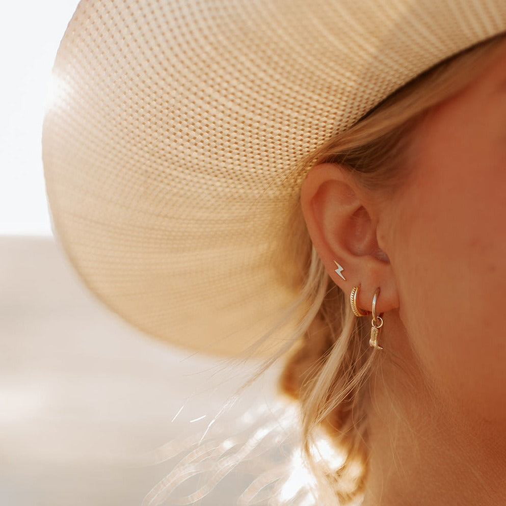 Gold-tone braided hoop earring worn beside a small dangling earring.