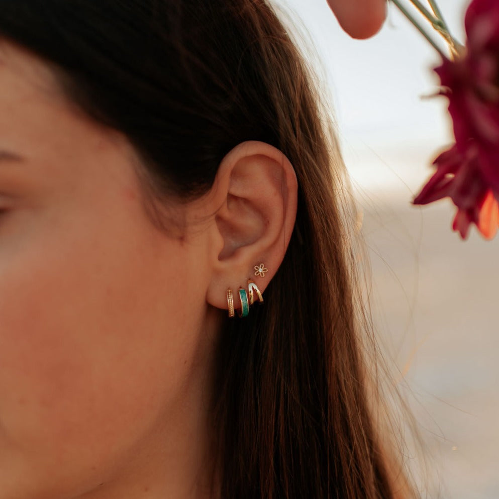Gold flower stud worn above several small hoop earrings.