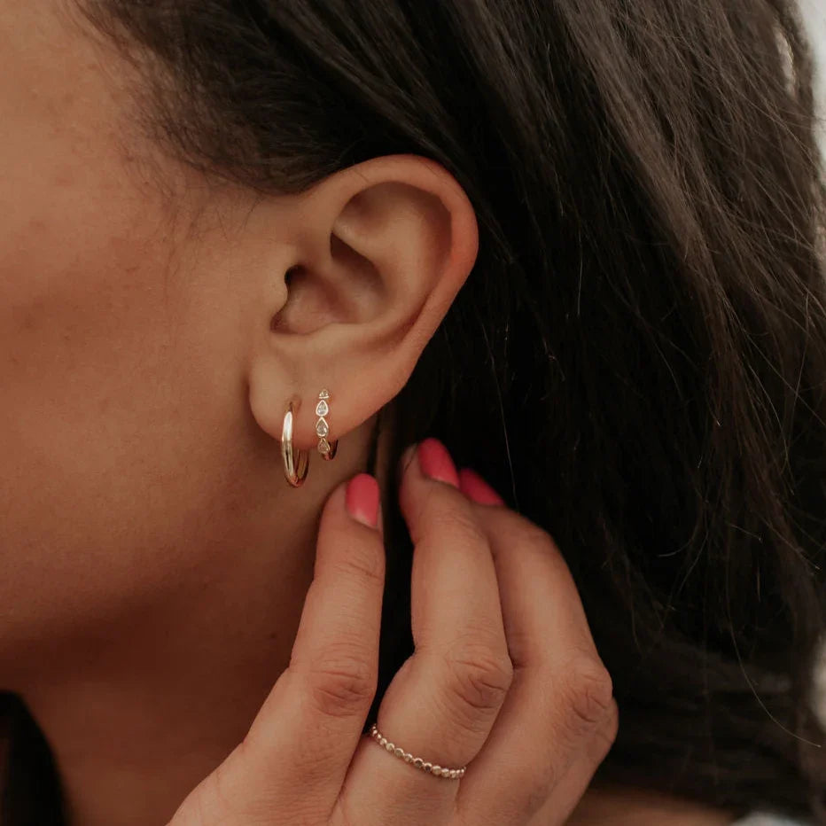 Gold raindrop hoop earrings shown worn on an ear