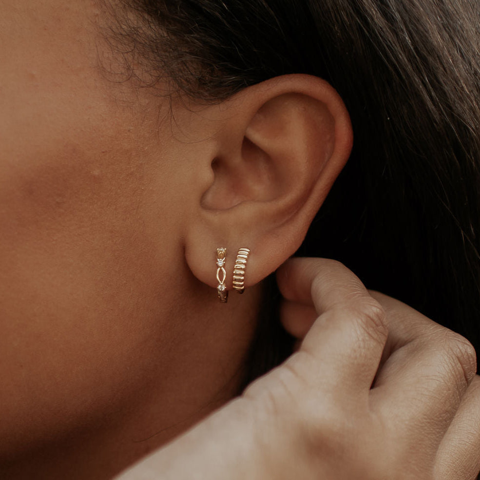 Gold lace huggie hoop earring worn on the earlobe, with a small openwork pattern