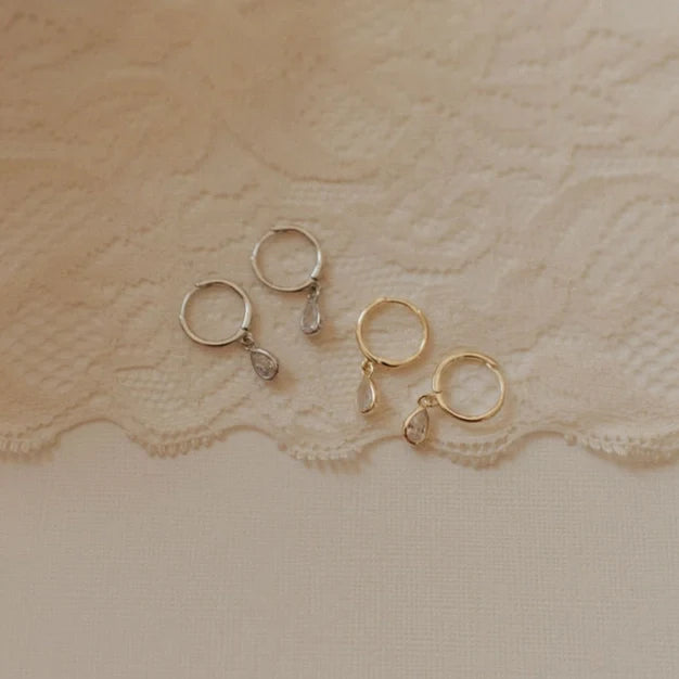 Gold and silver hoop earrings with dangling teardrop stones.