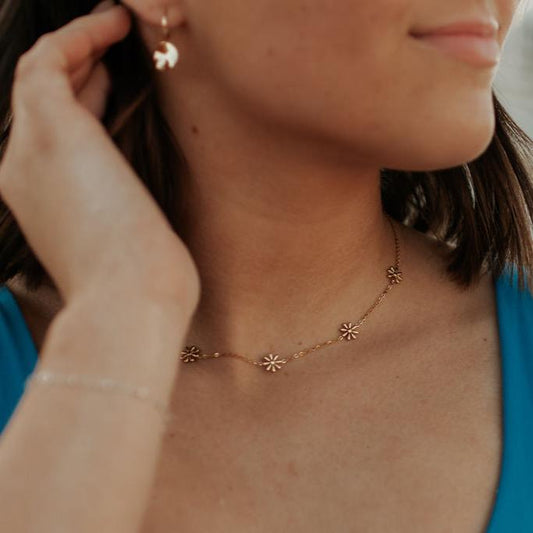 Gold floral necklace with small daisy charms, worn at the neckline