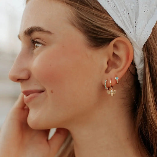 Gold-tone turquoise hoop earrings worn with a dangling charm