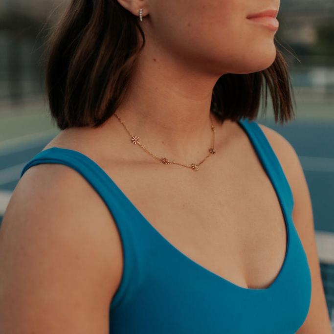 Gold daisy charm necklace worn close to the neckline