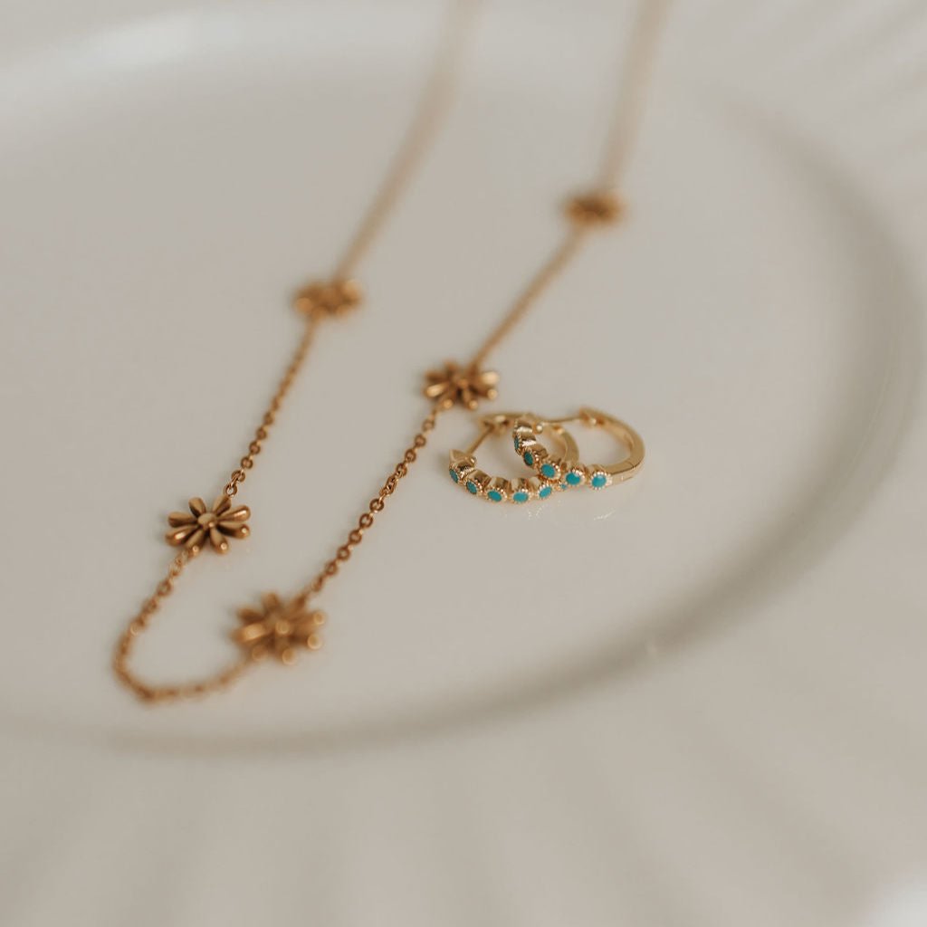 Gold-tone turquoise hoops beside a floral chain necklace