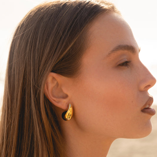 Gold-tone teardrop stud earring on ear, smooth curved drop with slim post-back.