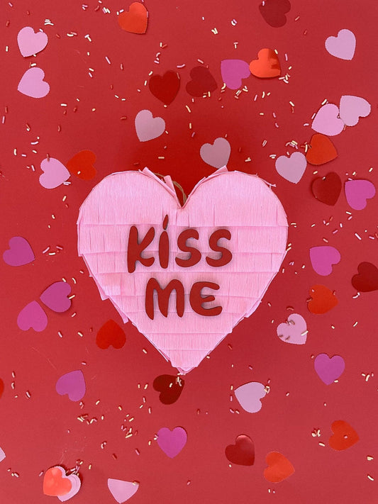 Pink heart piñata with “KISS ME” text and small heart confetti design