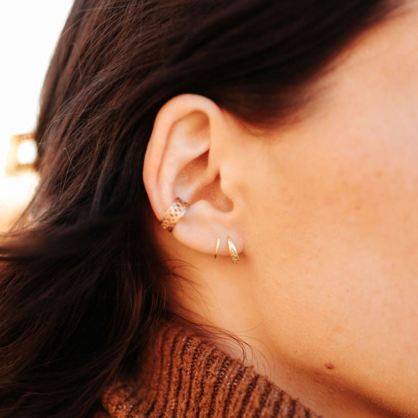 Gold double twist earrings worn in the lower earlobe, shown close up.