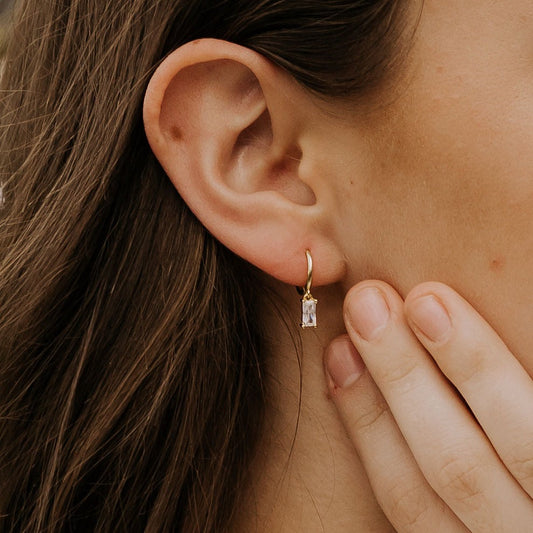 Gold dangle hoop earring with a clear baguette-cut stone, worn on the ear