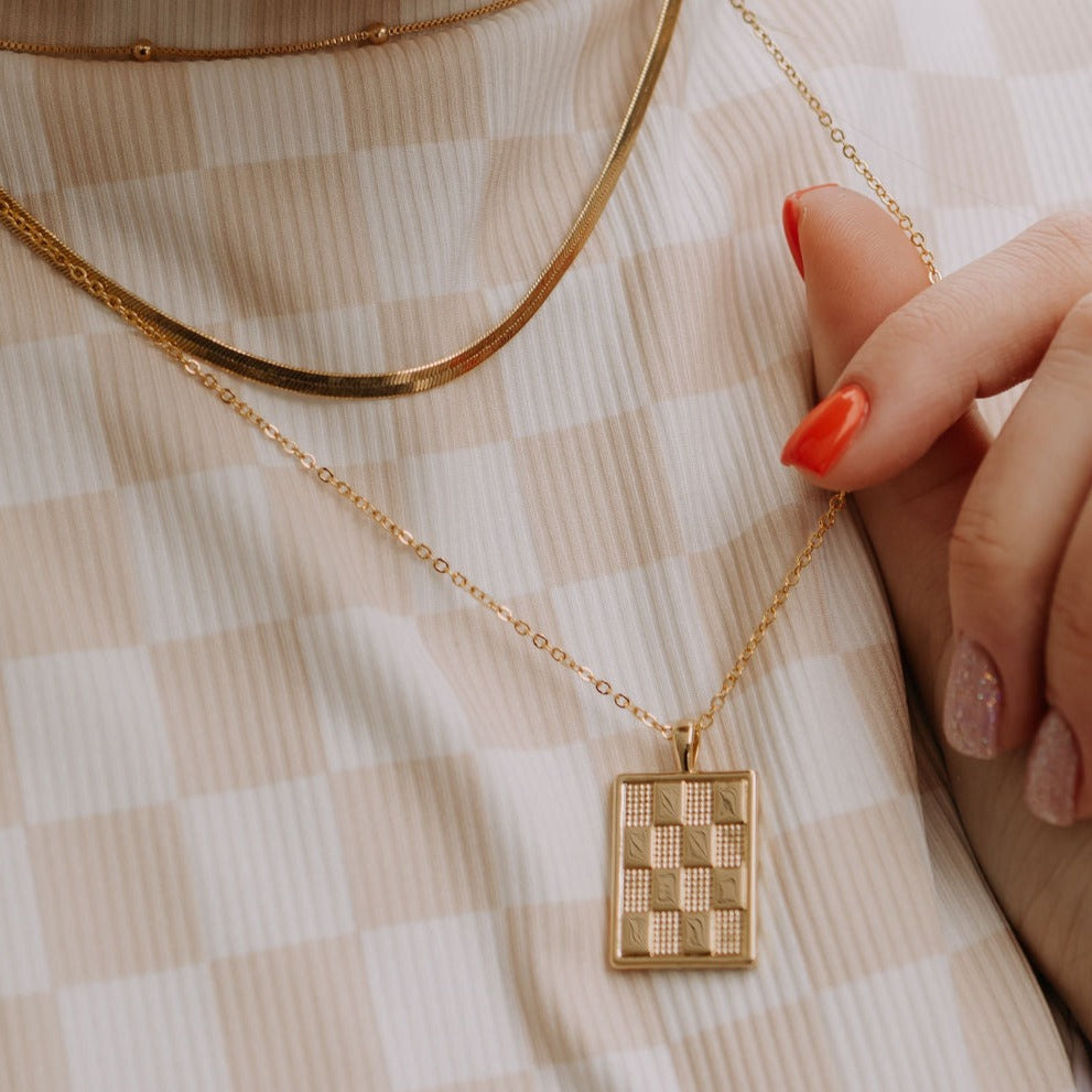 Close-up of the gold necklace's rectangular checkerboard pendant and fine chain.