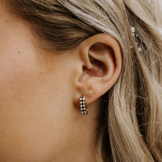 Gold hoop earring worn on an ear, showing its black-and-white diamond pattern