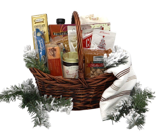 Large wicker gift basket with holiday snacks, wrapped blanket, and pine accents.